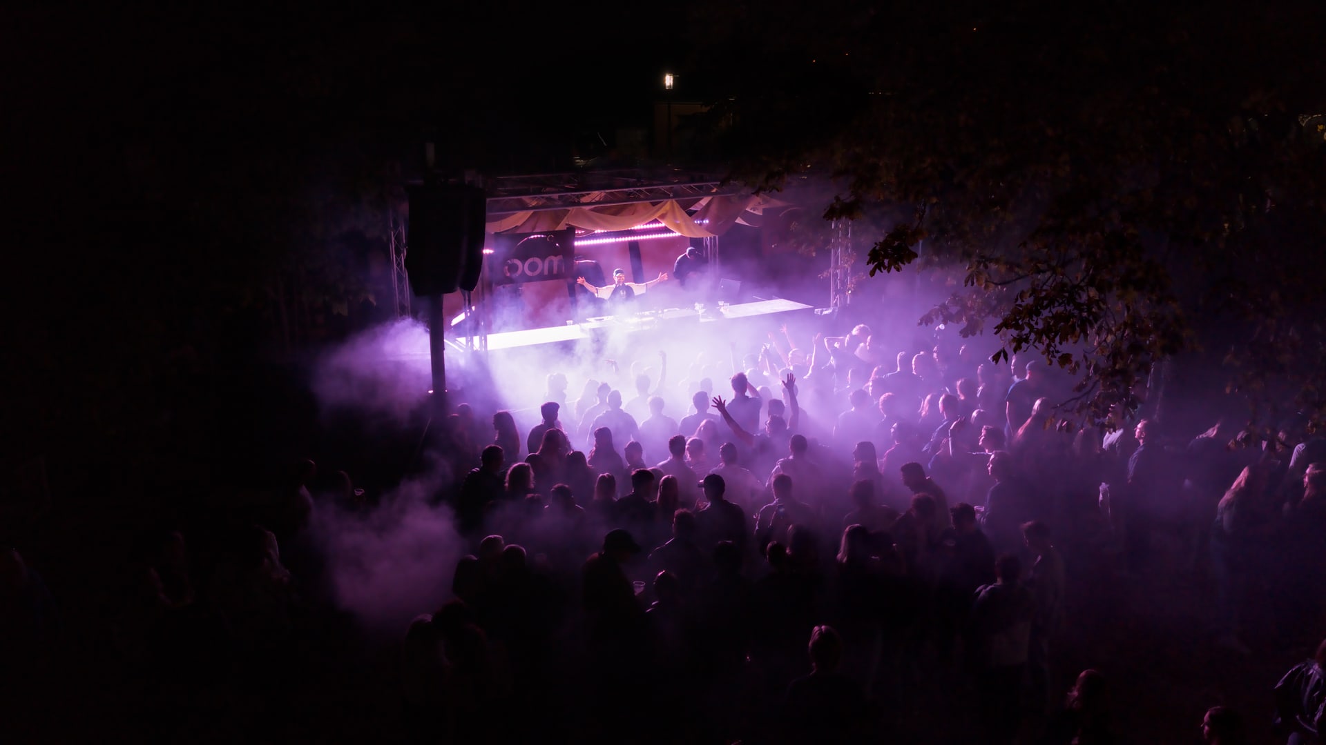 Luftaufnahme eines Open-Air-Festivals bei Nacht mit violettem Bühnennebel
